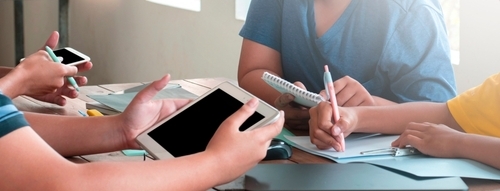 A Shutterstock licensed photo of students' hands with different technology devices strategizing together.